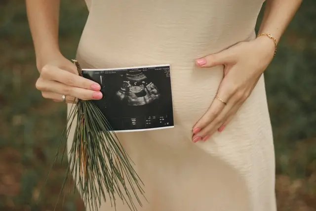 Photo ventre d'une femme debout avec une image d'une échographie d'un bébé tenu avec la main devant son ventre